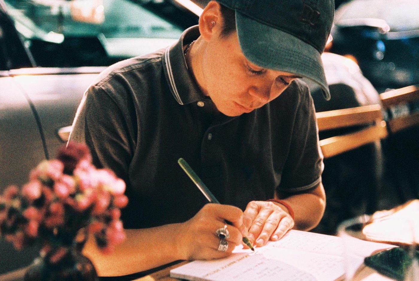 Filip writing in a notebook beside a vase of flowers.