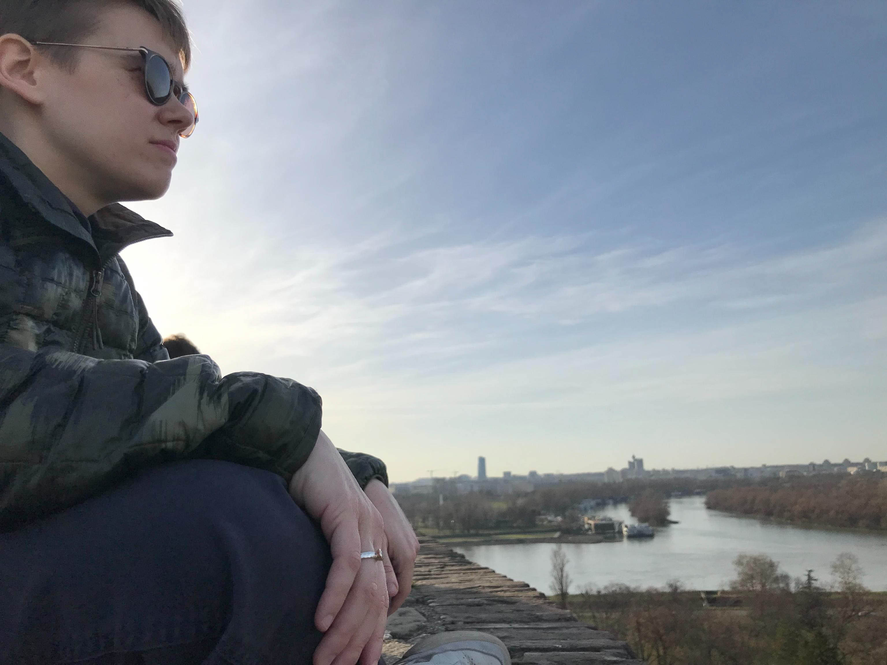 Filip sitting on a wall above a river at dusk.
